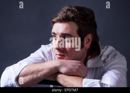 Uomo bello in posa di una camicia bianca su sfondo scuro in studio. Foto Stock