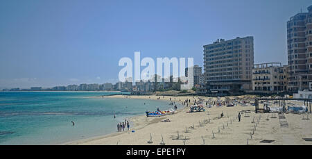 Appartamenti e alberghi abbandonati sulla spiaggia di Varosha Famagusta nella distanza mentre i turisti per le vacanze relax sulla spiaggia nelle vicinanze. Foto Stock