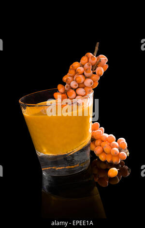 Bacche di olivello spinoso e bacche di olivello spinoso succo di frutta in vetro isolato su sfondo nero. Vita sana, sistema immunitario booth. Foto Stock