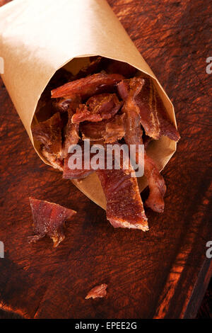 Carni bovine a scatti. Asciugare la carne di manzo a scatti sul tagliere di legno su sfondo di legno. La carne secca, rustica in stile country. Deliziosi piatti a base di carne Foto Stock