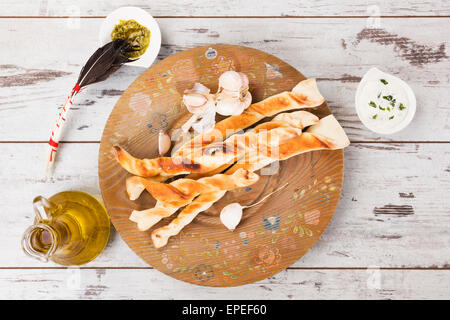 Per la produzione di grissini Pizza bianca su sfondo di legno con olio d'oliva e aglio e basilico dip. Culinario mangiare pizza. Foto Stock