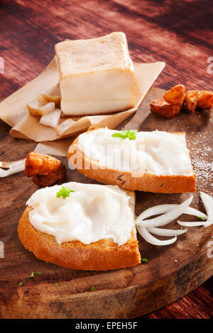 Le fette di pane con il lardo di maiale scratchings e pancetta sul tagliere di legno su sfondo marrone. Cucina tradizionale di mangiare. Foto Stock