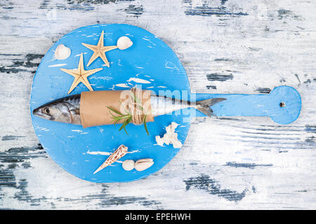 Freschi e deliziosi sgombro pesce sulla cucina in legno bordo con stella di mare, il Seashell su bianco e blu texture di sfondo di legno. Foto Stock