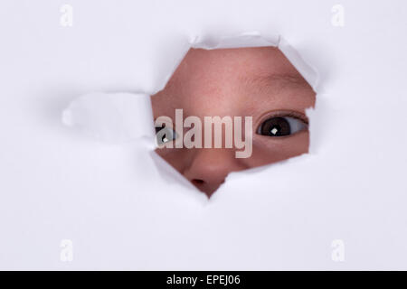 Baby ist neugierig und schaut durch ein Loch Foto Stock