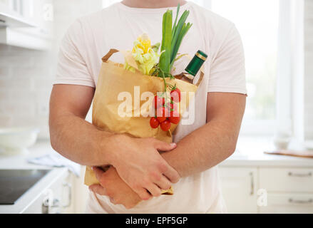 Uomo con sacchetto di carta pieno di negozi di generi alimentari in cucina Foto Stock