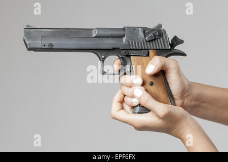 Mani femminili con la pistola isolato su sfondo grigio Foto Stock