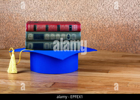 Graduazione mortarboard sulla parte superiore della pila di libri su sfondo astratto della parete Foto Stock