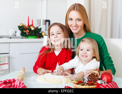 Due ragazze adorabili con la madre la cottura biscotti di Natale in cucina Foto Stock