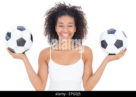 Bella ragazza con acconciatura afro sorridente in telecamera tenendo palloni da calcio Foto Stock