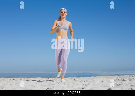 Bionda sportiva sulla spiaggia jogging verso la telecamera Foto Stock