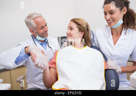 Dentista stringe la mano con il suo paziente nella sedia accanto a assistant Foto Stock