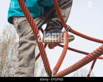 Giovani sicuri footed boy arrampicata corda spidery apparecchiatura in un parco giochi norvegese Foto Stock