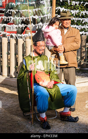 Un padre e una figlia che posano accanto ad un uomo seduto vestito da Dio pescatore, Ebisu, al festival di nuovo anno al santuario di Shinto Nishinomiya. Foto Stock