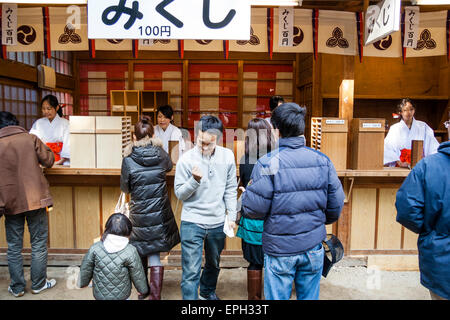 La gente che compra omikuji, carte di fortuna, al santuario di Shinto a Nishinomiya a nuovo anno. Un giovane, che cammina verso lo spettatore, pugno clenching, estatico. Foto Stock