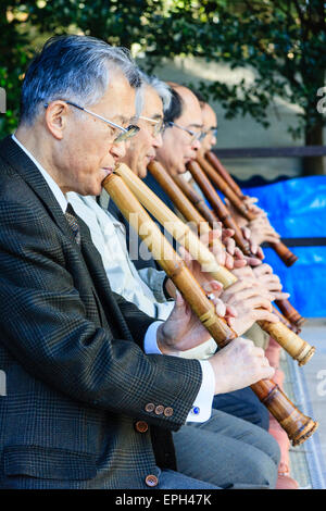 Giappone, Nishinomiya, Santuario di Koshiki-wa. Fila di anziani, uomini anziani in giacca inginocchiati su un palco che suona flauto recital per le celebrazioni del nuovo anno. Foto Stock