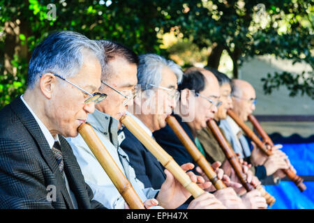 Giappone, Nishinomiya, Santuario di Koshiki-wa. Fila di anziani, uomini anziani in giacca inginocchiati su un palco che suona flauto recital per le celebrazioni del nuovo anno. Foto Stock