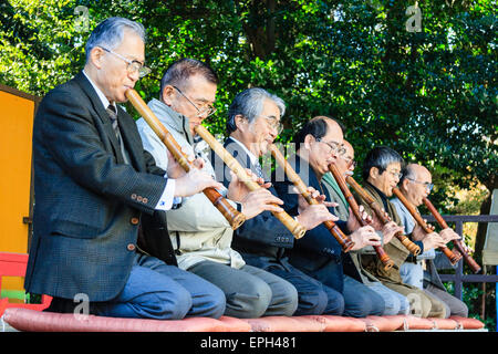 Giappone, Nishinomiya, Santuario di Koshiki-wa. Fila di anziani, uomini anziani in giacca inginocchiati su un palco che suona flauto recital per le celebrazioni del nuovo anno. Foto Stock