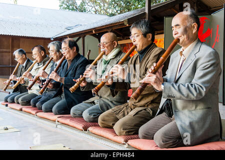 Giappone, Nishinomiya, Santuario di Koshiki-wa. Fila di anziani, uomini anziani in giacca inginocchiati su un palco che suona flauto recital per le celebrazioni del nuovo anno. Foto Stock