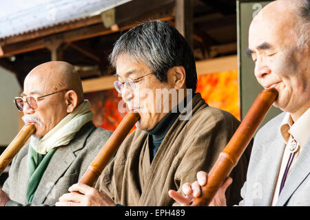 Giappone, Nishinomiya, Santuario di Koshiki-wa. Fila di anziani, uomini anziani in giacca inginocchiati su un palco che suona flauto recital per le celebrazioni del nuovo anno. Foto Stock