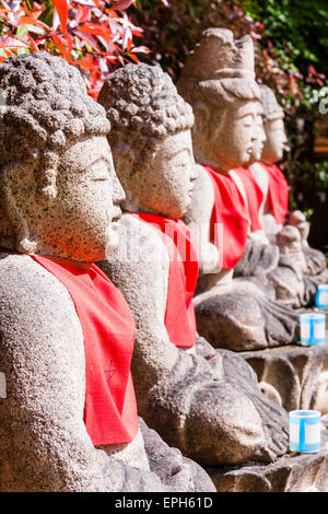 Primo piano vista lungo quattro statue di bosatsu Jizo con i bibs rossi in asunlight, all'aperto al tempio di Suma Dera a Suma, Giappone. Foto Stock