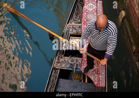 Venezia, Italia - 24 Aprile 2013: gondoliere in classic striped shirt spinge tradizionale gondola lungo le acque del canale. Foto Stock