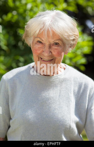 Testa e spalle il ritratto di capelli grigi sorridenti donna senior o la nonna in piedi nella luce del sole in giardino. Foto Stock