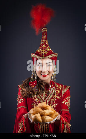 Woman in Red nazionale costume kazako tenendo la piastra con baursak pane alla celebrazione Nauryz Foto Stock