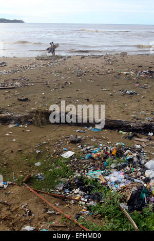 I surfisti a piedi lungo la spiaggia coperta di immondizia di plastica e di altri rifiuti di Sumatra, Indonesia Foto Stock