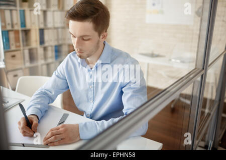 Imprenditore serio seduto da scrivania e rendere note Foto Stock