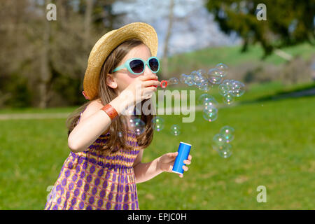 Una bambina con occhiali da sole rendendo le bolle di sapone Foto Stock