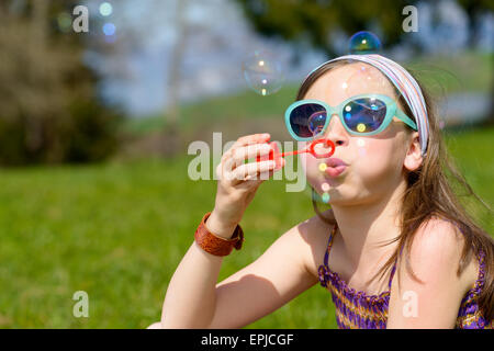 Una bambina con occhiali da sole rendendo le bolle di sapone Foto Stock