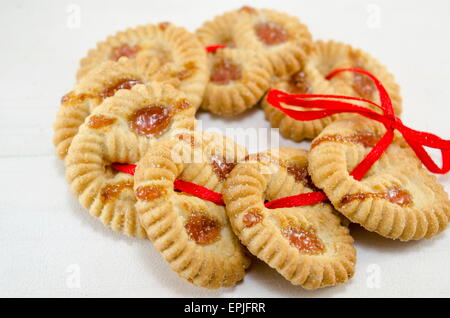 Biscotti da tè riempita con marmellata di albicocche su bianco collegato con un nastro rosso Foto Stock