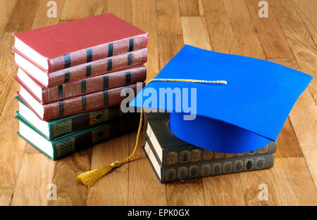 Graduazione mortarboard sulla parte superiore della pila di libri sullo sfondo di legno della parete Foto Stock