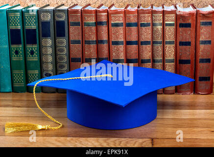 Graduazione mortarboard sulla parte superiore della pila di libri su sfondo astratto della parete Foto Stock