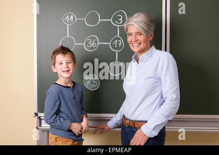 Maestro sorridente e schoolboy alla lavagna con problema aritmetico Foto Stock