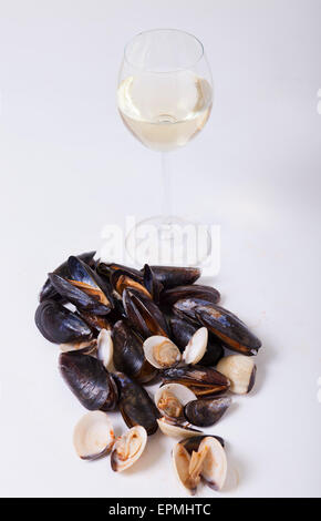 Cozze e cardidi con un bicchiere di vino bianco contro uno sfondo bianco Foto Stock