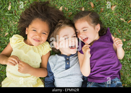 Tre bambini che giace sulle loro spalle sull'erba, guardando verso l'alto e ridere. Foto Stock