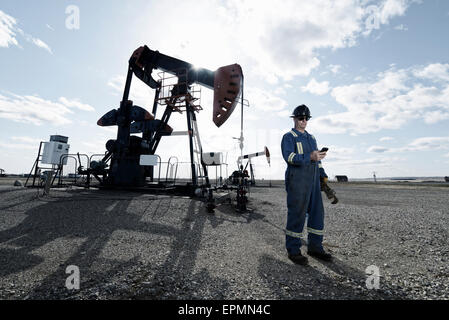 Un uomo in tuta e elmetto in una pompa jack in terreno aperto in corrispondenza di un olio nel sito di estrazione. Foto Stock