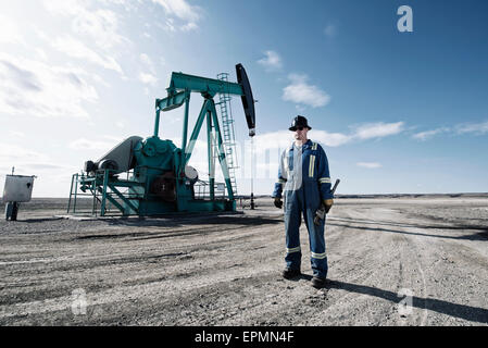 Un uomo in tuta e un elmetto con una chiave dinamometrica di grandi dimensioni lavorando a un olio nel sito di estrazione. Foto Stock