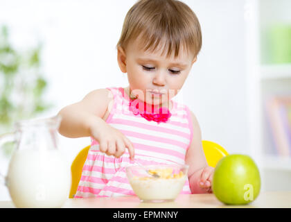 Carino bambina mangia il cibo sano seduta a tavola in vivaio Foto Stock