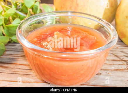 Un vaso di vetro pieno di marmellata di mele, di fronte alle mele ed erbe aromatiche Foto Stock