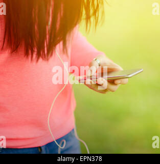 Ragazze mani tenendo il telefono cellulare mentre ascolti la musica contro la natura verde sullo sfondo Foto Stock