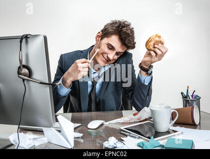 Giovane uomo d affari a parlare al telefono mentre si tiene il burger in una mano e la matita in altri guardando giù sorridente / moderno o Foto Stock