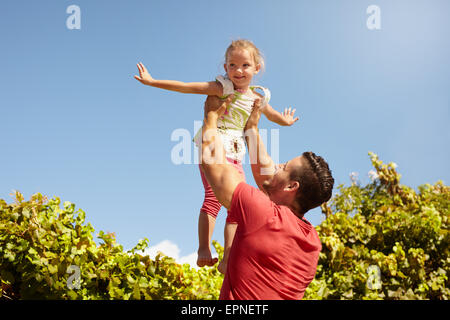 Bambina fingendo di essere un velivolo come suo padre il suo ascensore nell'aria. Padre tenendo la sua figlia fino ad alta contro il cielo. Foto Stock