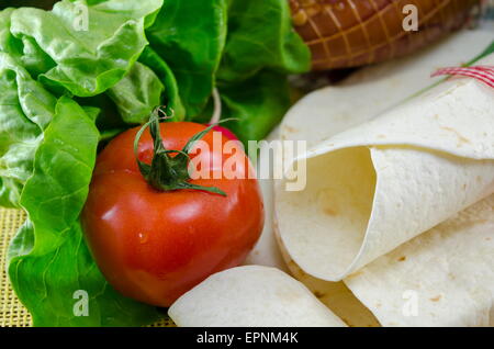 Svuotare tortillas legate con un nastro rosso su un tavolo con il pomodoro, la lattuga e prosciutto Foto Stock