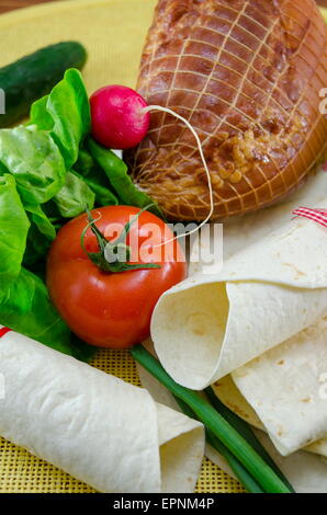 Svuotare tortillas legate con un nastro rosso su un tavolo con il pomodoro, la lattuga e prosciutto Foto Stock