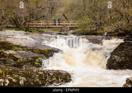 Due escursionisti attraversare il ponte che attraversa la parte superiore scende di Aira Beck, al di sopra di Aria forza, vicino a Ullswater, Lake District, Cumbria Foto Stock