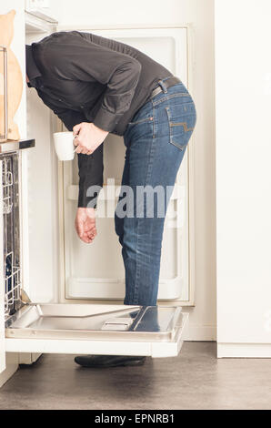 L'uomo bloccato la sua testa nel frigorifero per cercare qualcosa da mangiare o da bere. Egli è in possesso di una tazza di caffè in mano. Conceptual Foto Stock