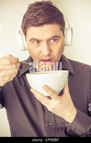 Uomo occupato con un auricolare wireless per telefono cellulare mangiare cereali per la prima colazione. Foto Stock