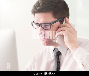 Imprenditore parlando al cellulare e a lavorare con il computer in ufficio. Foto Stock